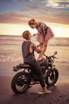 girlfriend standing on motorcycle and touching boyfriend chin on ocean beach