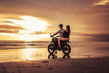 Fototapeta na wymiar affectionate couple sitting on motorcycle on ocean beach during sunrise