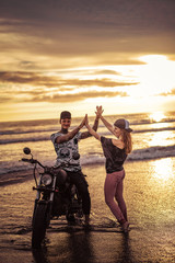 Fototapeta na wymiar couple giving high five near motorcycle on ocean beach