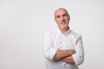 Confident senior man in white t-shirt crossing hands on chest and looking at camera