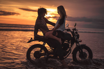 Fototapeta na wymiar girlfriend sitting on shirtless boyfriend on motorbike at beach during sunset