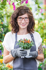 Gärtnerin im Gewächshaus hält lächelnd einen Topf mit Zierpaprika in den Händen