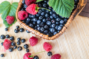 A basket with blueberries and raspberries on wooden background
