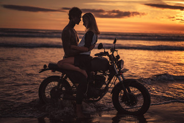 Fototapeta na wymiar seductive couple hugging on motorbike at beach during sunset