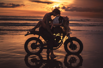 Fototapeta na wymiar sexy couple hugging on motorbike at beach during sunset