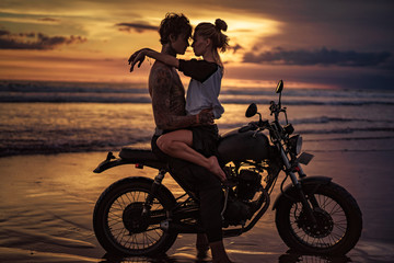 Fototapeta na wymiar Passionate couple cuddling on motorcycle at beach during sunset