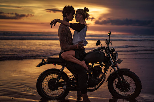 Passionate couple cuddling on motorcycle at beach during sunset