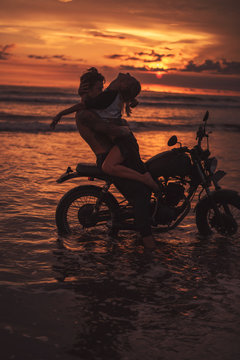 sexy boyfriend and girlfriend hugging on motorcycle at beach during sunset