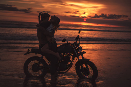 sexy couple hugging on motorcycle at beach during sunset