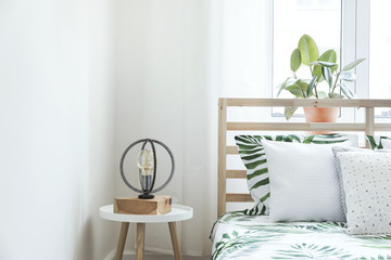 Modern and stylish bedroom with plants, design lamp and floral pattern bedding. Bright and sunny space with wooden parquet and white walls.