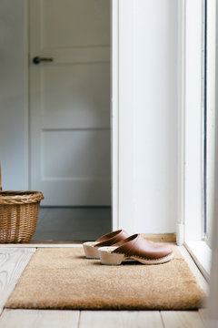 A pair of brown leather clogs standing in front of a door on a brown mat.