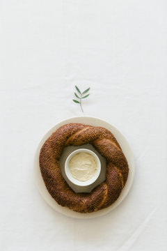 A simit, a Turkish round bagel topped with sesame seeds, waiting to be spread with the hummus from the cup inside it.