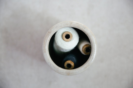A collection of vintage bobbins in a grey vase seen from above all in neutral muted colors.