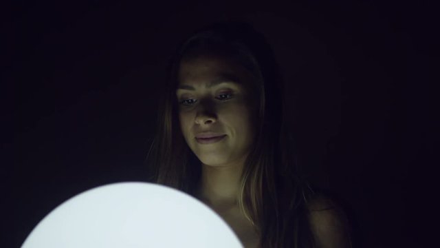 Attractive young happy woman holding glowing ball at night while smiling 