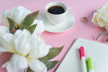 A cup of coffee and notebook on the pink background with white peony. Planning.