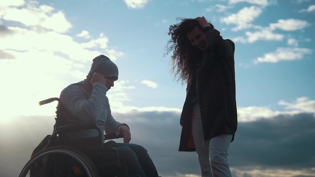 Young woman with disabled man in a wheelchair talking outdoors at sunset