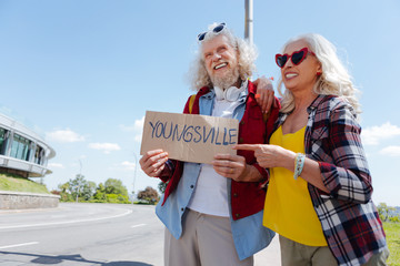 Ready to travel. Delighted aged woman pointing at the sign while travelling together with her...