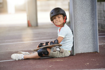 Young boy with skateboard sitting on the ground
