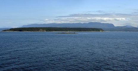 Rebecca Rock with warning light for mariners with Harwood Island in the background; in the waters of the Strait of Georgia of the shores of Powell River British Columbia Canada 