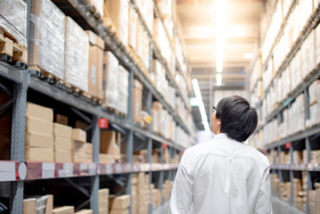 Young Asian man standing between cardboard box shelves in warehouse choosing what to buy, shopping warehousing concept