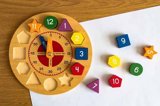 Toy wooden clock on a sheet of white paper, on a wooden background