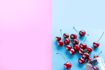 Sweet cherry ripe in a glass Cup scattered on a blue background, summer, fruit, healthy food. Flat lay and copy space.