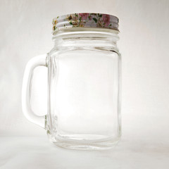 Empty clear mason jar with a handle and a lid on a white background. Transparent glass mug for summer drinks close-up