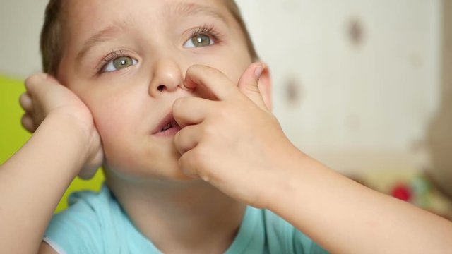 A thoughtful child picks his finger in the nose in a slow motion