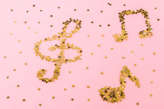 Musical notes of starry golden confetti lying on a pink pastel background.