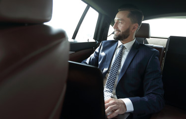 Smiling businessman with laptop sitting in car