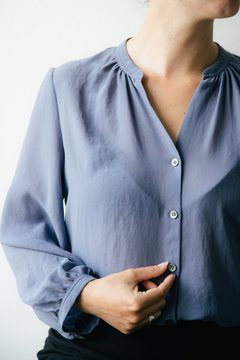 Portrait of a woman in a lavender blue shirt touching one of the buttons.