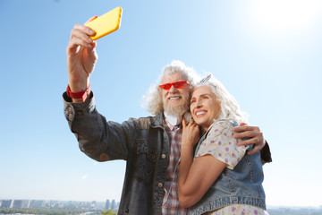 Our photo. Cheerful positive man holding a smartphone while taking a photo of him and his wife