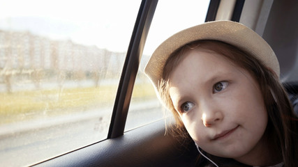 Little girl looking out from car window at sunny day.