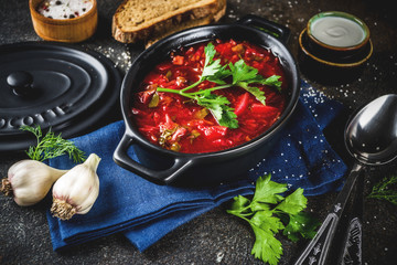 Ukrainian Russian traditional hot dish - borsch soup, with greens, garlic, rye bread, on a dark table,