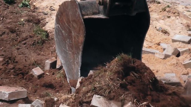 excavator bucket destroys the old road out of bricks.close-up