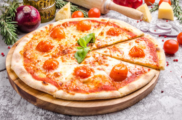 Homemade Meat Loves Pizza with basil, cherry tomatoes, pepperoni sausage, bacon, onions, cucumber, cheese on a wooden board over stone table background, restaurant menu concept. Italian food style