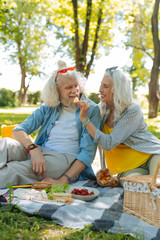 Its tasty. Nice joyful woman feeding her husband while having a picnic with him