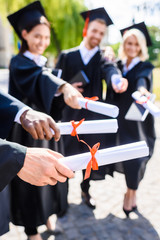 cropped shot of young graduated students holding rolled diplomas