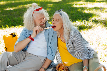 You must try. Happy nice man feeding his wife while having a picnic together with her