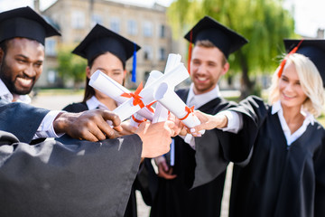 young graduated students making team gesture with rolled diplomas