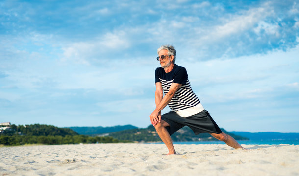 Senior man doing stretching exercises on the beach