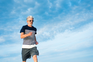 Senior man running against cloudy sky
