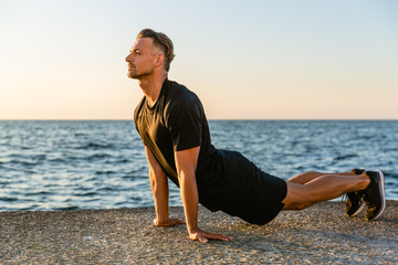 Fototapeta na wymiar handsome adult sportsman doing backbend while stretching on seashore