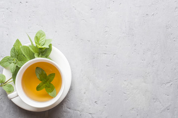 Cup of tea with fresh mint leaves on grey concrete background. Copy space