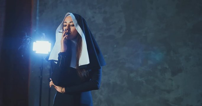 Beautiful girl in the image of a nun with a cigarette in her hand