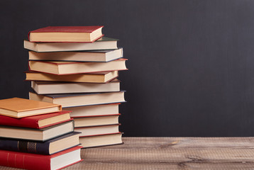 A pile of books  on the table. Blackboard background with copy space. Education concept.