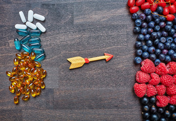 Pills and berries on a wooden table,