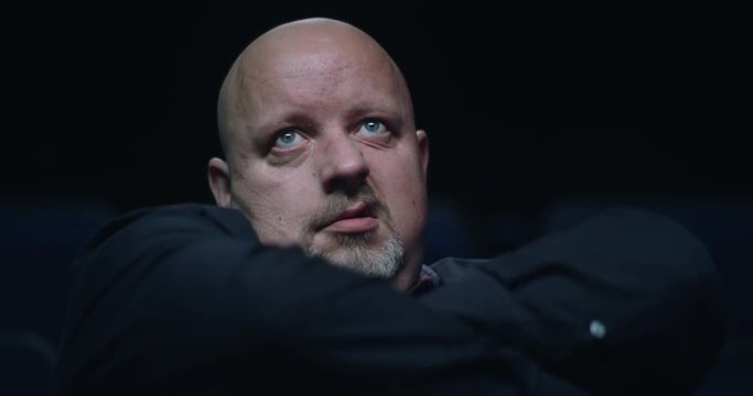 Bored movie theatre audience member crosses his arms, rolls his eyes and lets out a sigh.