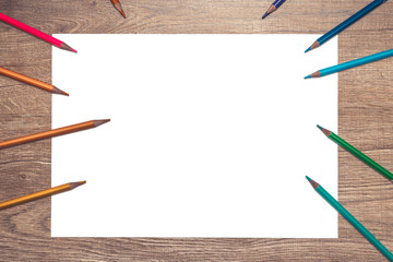 Colors pencils with blank on a sheet of paper on a wooden desk