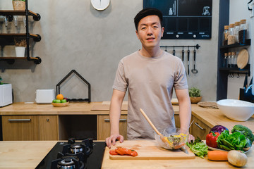 Young handsome asian man prepare salad food and cooking in the kitchen. Young asian male spend free...